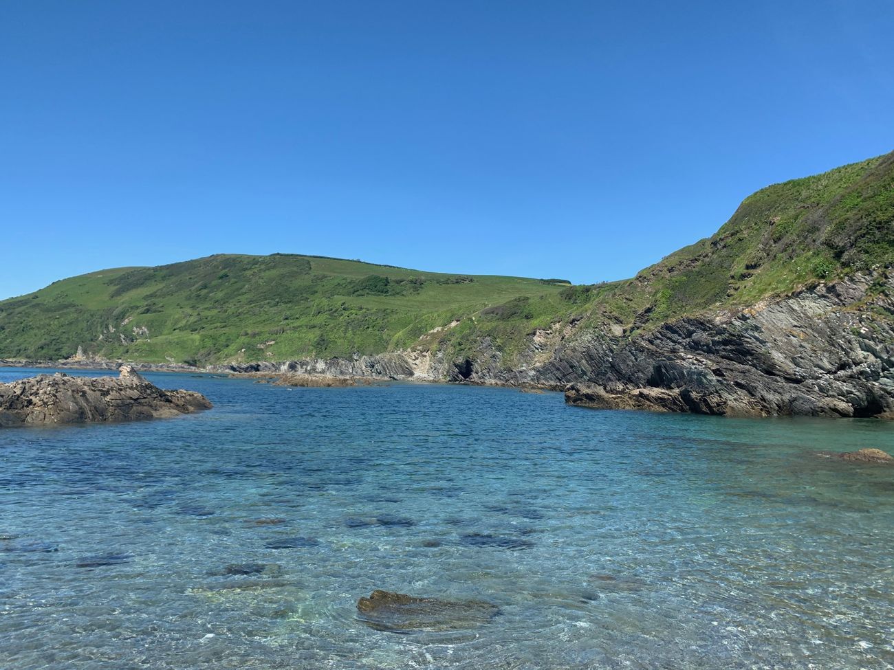 Clear turquoise water below a green Cornish headland